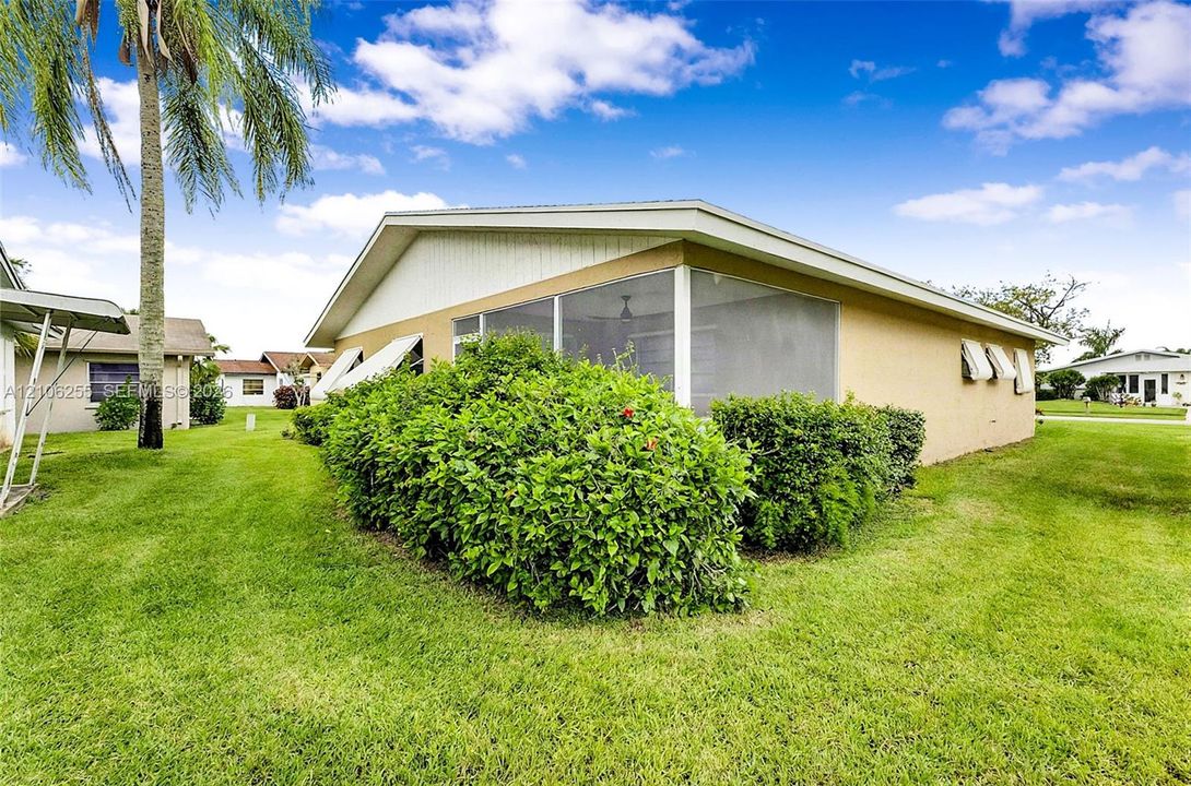 Stucco exterior residence featuring a screened-in lanai, decorative window awnings, and landscaped perimeter shrubbery set on a level lawn