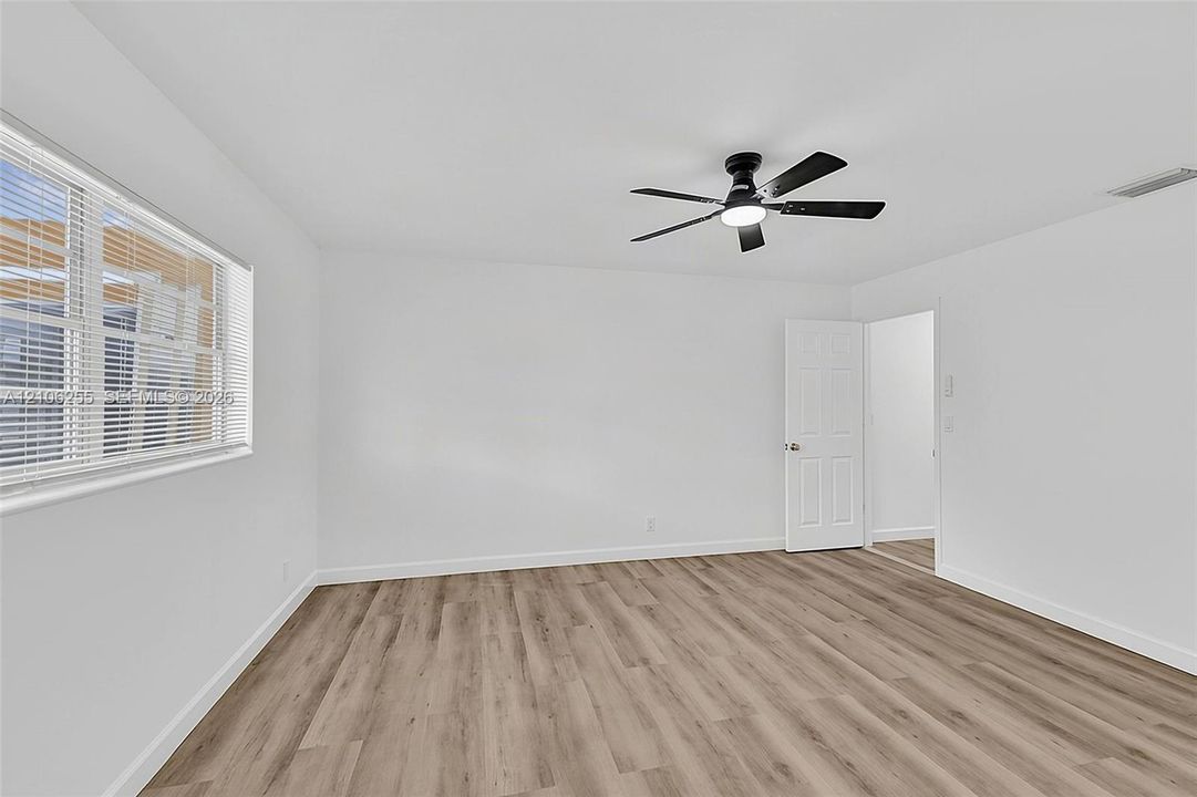Neutral interior featuring wood-finish flooring, white walls, a multi-blade ceiling fan with integrated lighting, and a six-panel interior door
