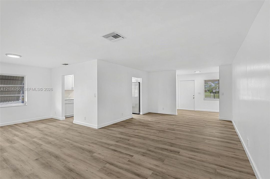 Open-concept interior featuring wood-finish flooring, crisp white walls, flush-mount lighting, and dual windows