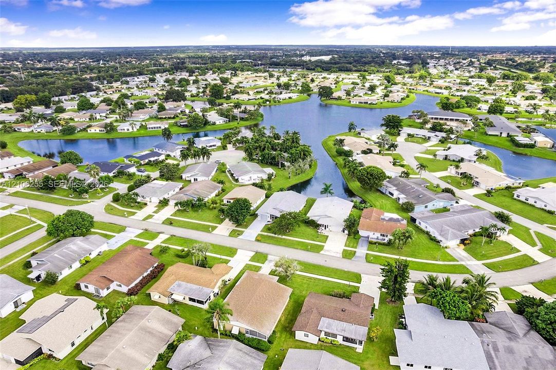 Aerial perspective of a residential community featuring a central waterway, manicured lawn areas, and mature landscaping