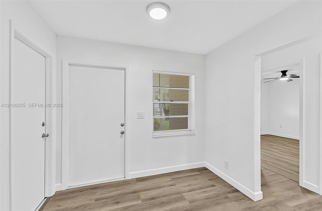 Neutral interior space featuring wood-finish flooring, a flush-mount ceiling light fixture, and horizontal blind window treatments