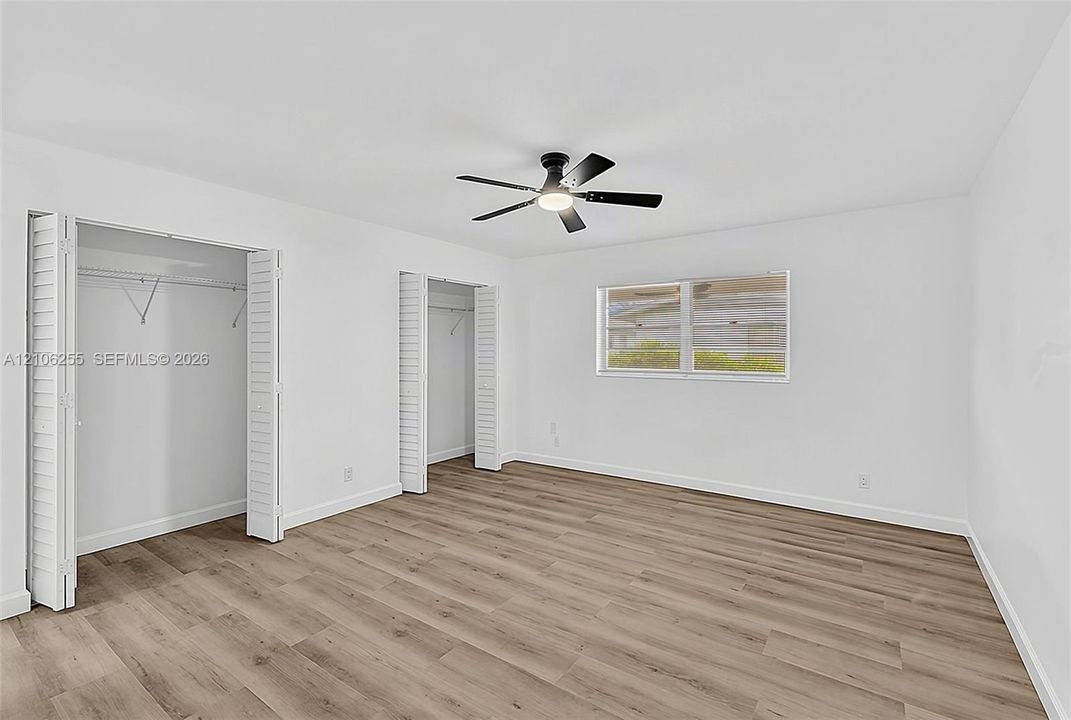 Neutral-toned wood-finish flooring, two closets with louvered folding doors, and a ceiling-mounted light fixture with fan