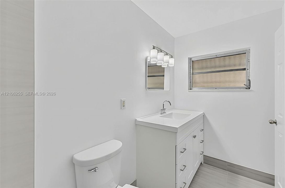 White vanity with integrated basin, multi-drawer storage, polished metal faucet, multi-bulb vanity light, and gray tile flooring