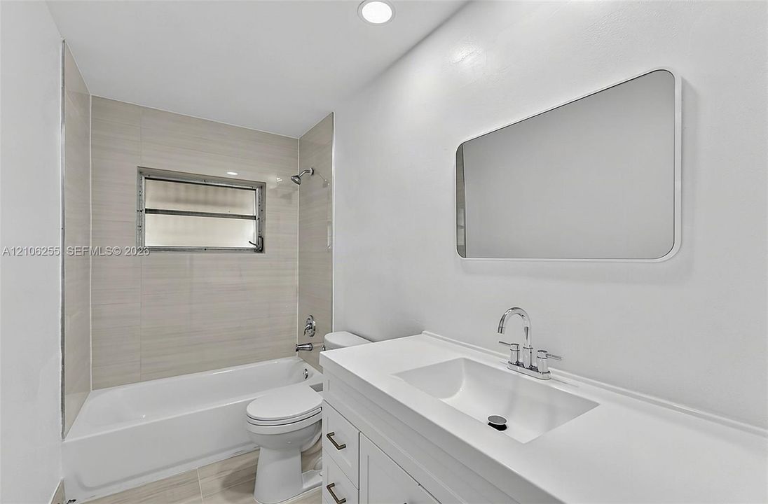 Bathroom featuring a white vanity with an integrated sink, rectangular mirror, recessed lighting, and a bathtub with neutral tile surround
