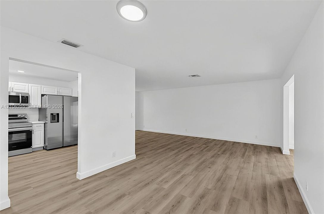 Open-concept interior featuring wood-finish flooring, recessed lighting, and a kitchen equipped with stainless steel appliances and white cabinetry