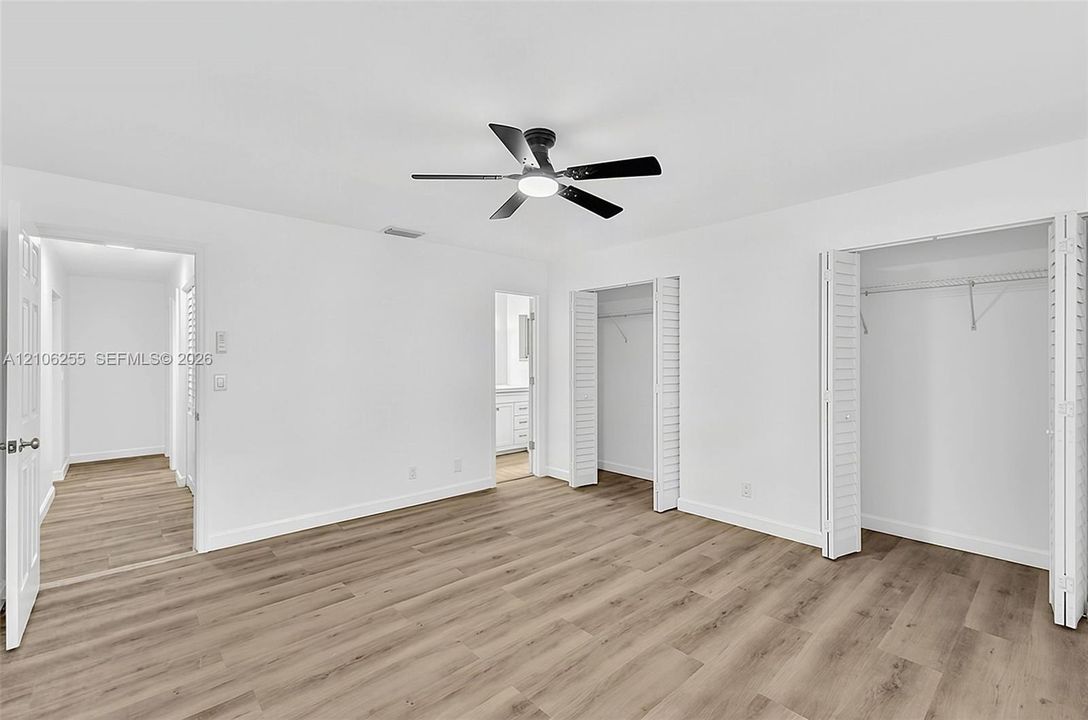 Room featuring wood-finish flooring, a matte black ceiling fan with an integrated light fixture, and dual closets with bi-fold doors