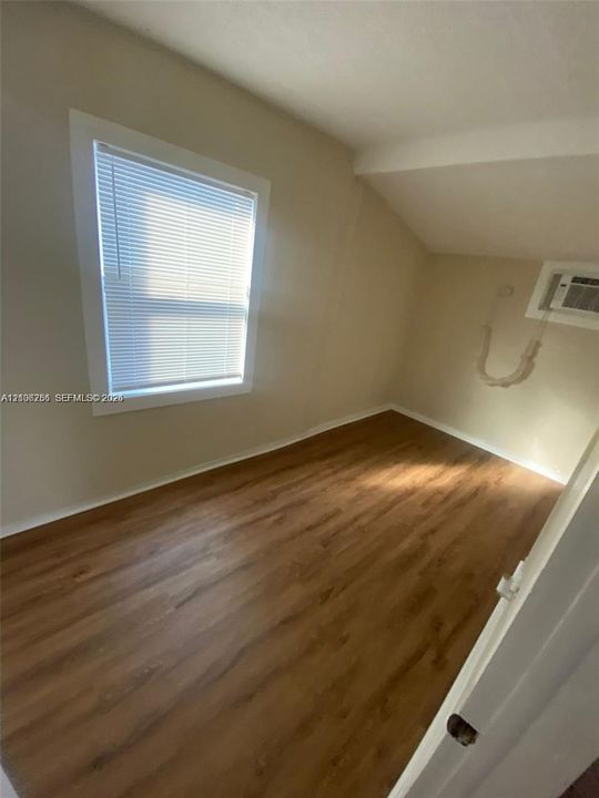 Neutral interior featuring wood-finish flooring, white window trim, and a wall-mounted unit
