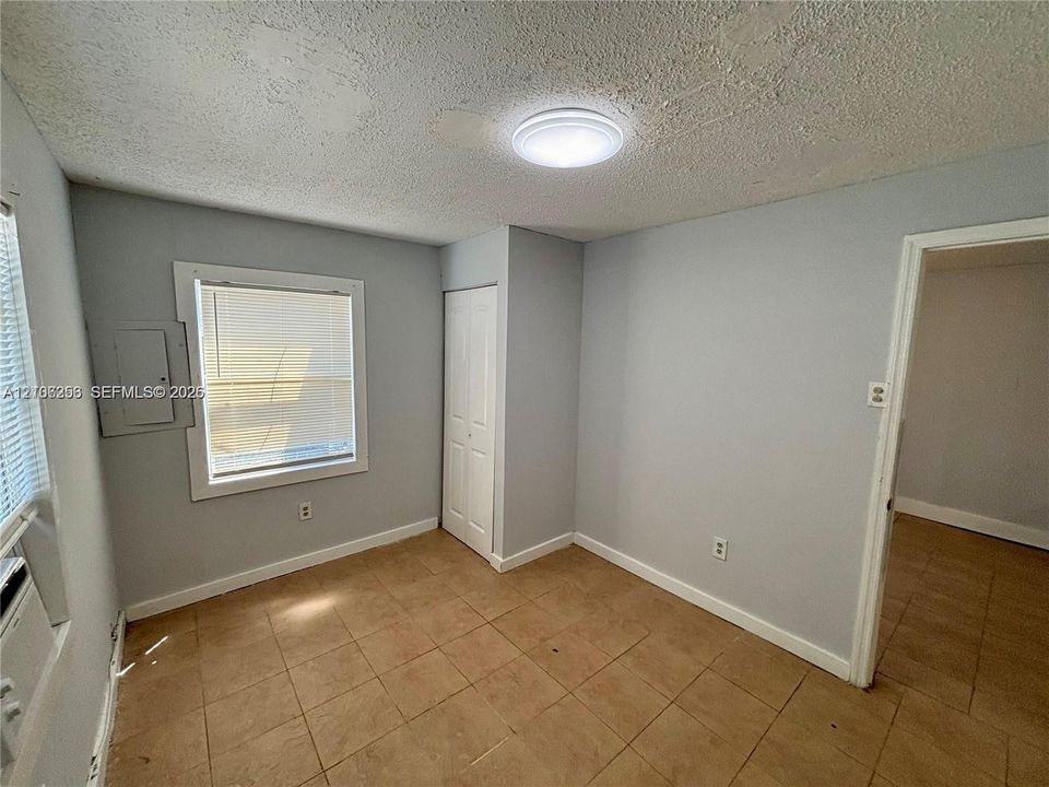 Neutral-toned interior space featuring light-colored tile flooring, flush-mount ceiling lighting, a white panel closet door, and a multi-pane window