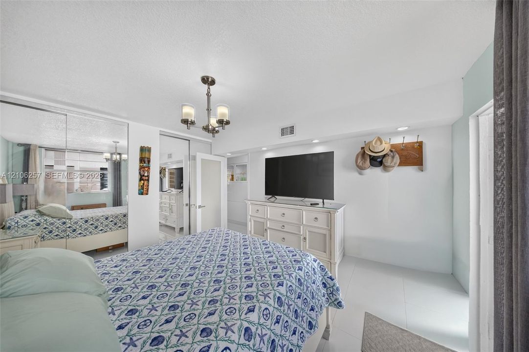 Room featuring polished tile flooring, full-wall mirrored closet doors, a multi-arm chandelier, and recessed ceiling lighting