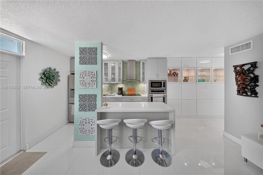 Kitchen featuring a central island with a quartz countertop, white cabinetry, integrated stainless steel appliances, a tile backsplash, and polished tile flooring. Lots of storage!