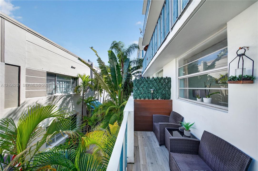 Rear Private balcony featuring wood-finish flooring, metal railing, privacy screening, and wall-mounted exterior lighting