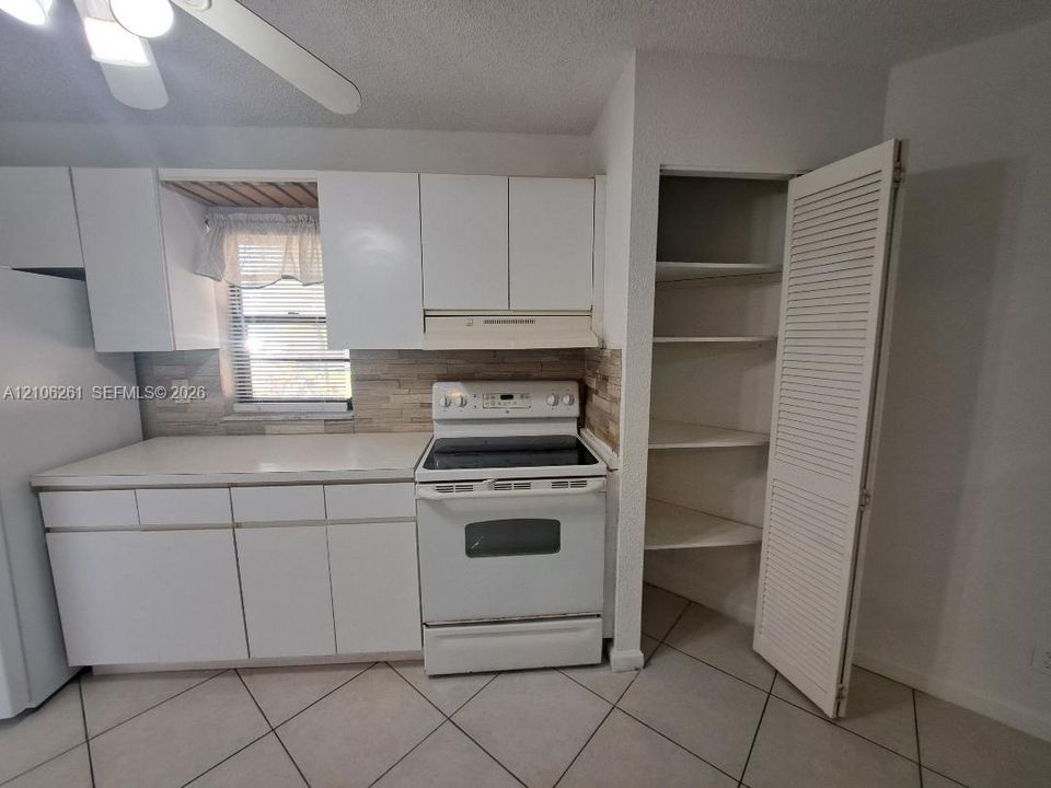 Kitchen featuring white cabinetry, light-toned stone-finish backsplash, integrated range, tiled flooring, and built-in louvered-door pantry