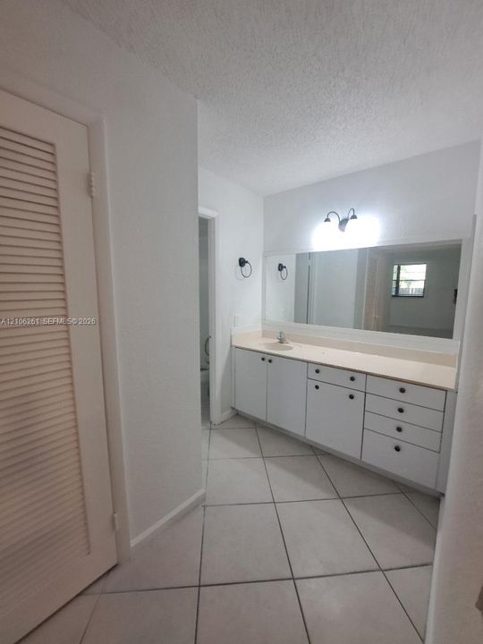 Vanity with extensive counter space and built-in cabinetry, large wall-mounted mirror, ceramic tile flooring, and louvered closet door
