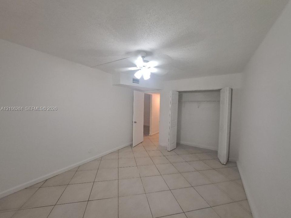 Neutral-toned tile flooring, ceiling fan with integrated lighting, and built-in closet with folding doors