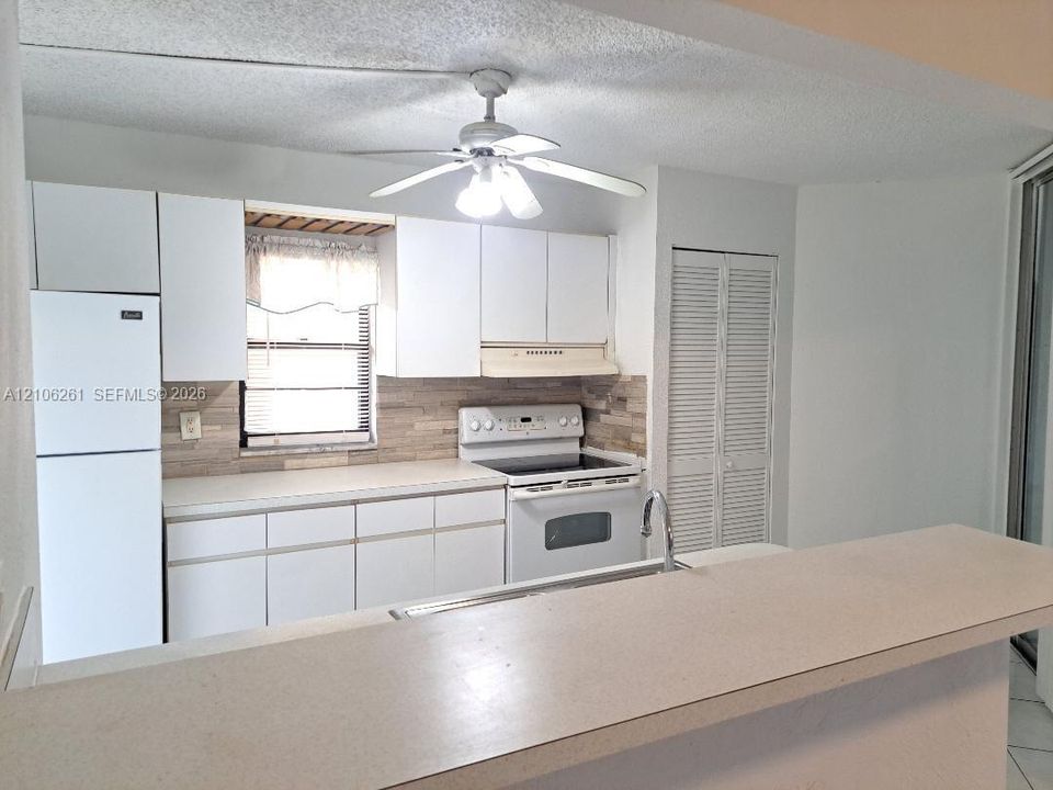 Kitchen featuring white cabinetry, stone-finish backsplash, built-in range, refrigerator, and solid surface breakfast bar