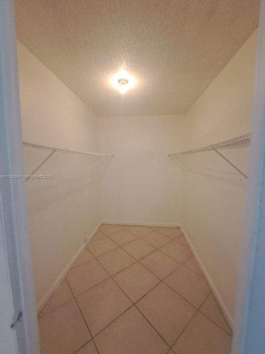 Walk-in closet featuring neutral tile flooring, dual-level white wire shelving, and a ceiling-mounted light fixture