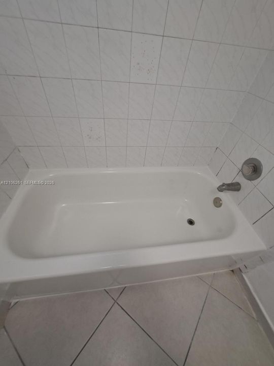 Bathtub with integrated faucet and metallic fixtures, surrounded by white wall-mounted ceramic tile and finished with diagonal-set floor tile