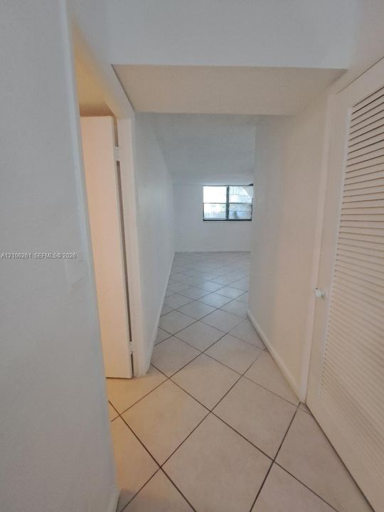 Neutral tile flooring laid on a diagonal pattern, interior louvered-style closet door, and window with white frame