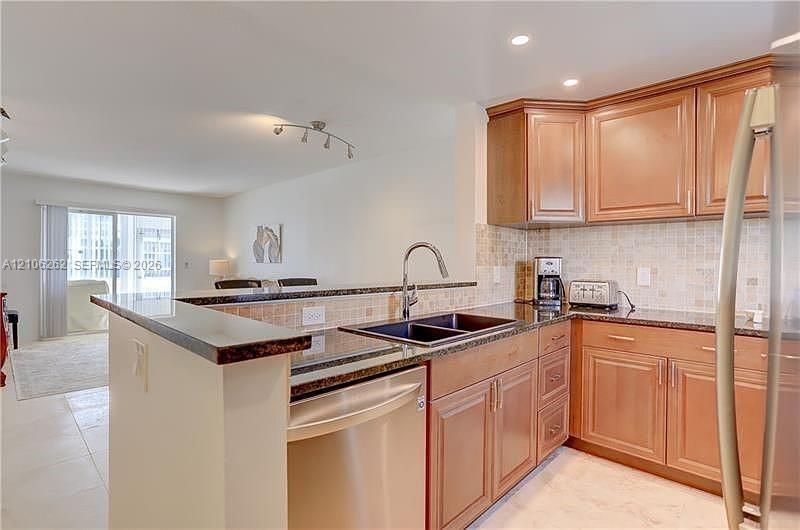 Kitchen featuring a pass-through counter, stainless steel appliances, wood cabinetry, and recessed lighting, finished with stone-tile flooring