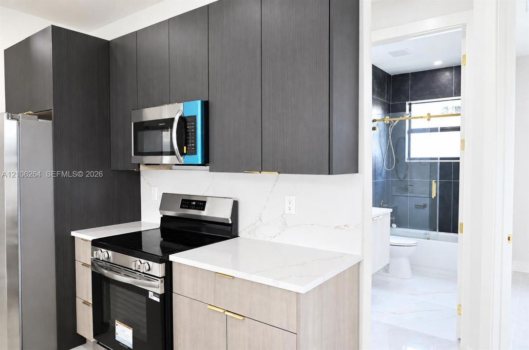 Kitchen featuring flat-panel two-tone cabinetry, quartz countertops, stainless steel appliances, and gold-tone hardware