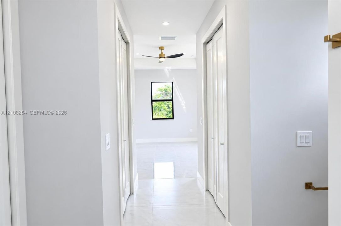 Hallway featuring light-toned tile flooring, recessed lighting, dual bi-fold closet doors, and metallic hardware fixtures