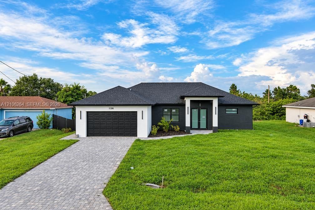 Modern exterior featuring high-contrast two-tone finish, dark-toned asphalt shingle roofing, dual-entry glass doors, and a decorative paver driveway