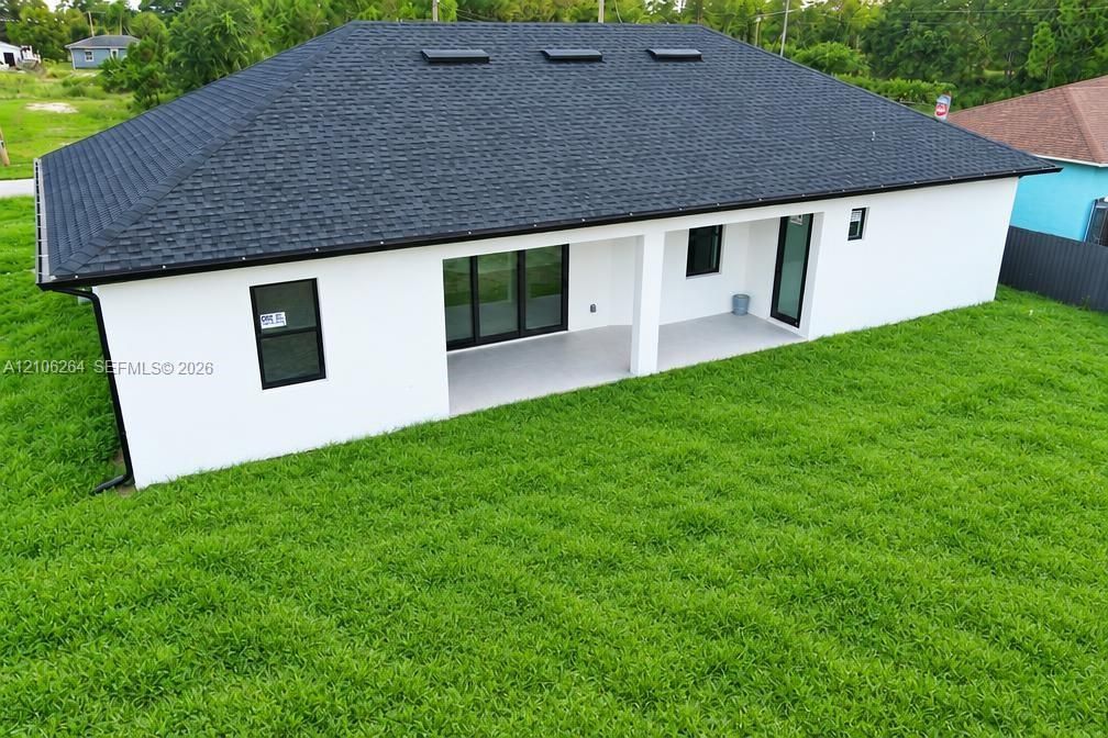Rear elevation featuring a hip roof with integrated skylights, a covered patio with concrete flooring, and black-framed windows and doors