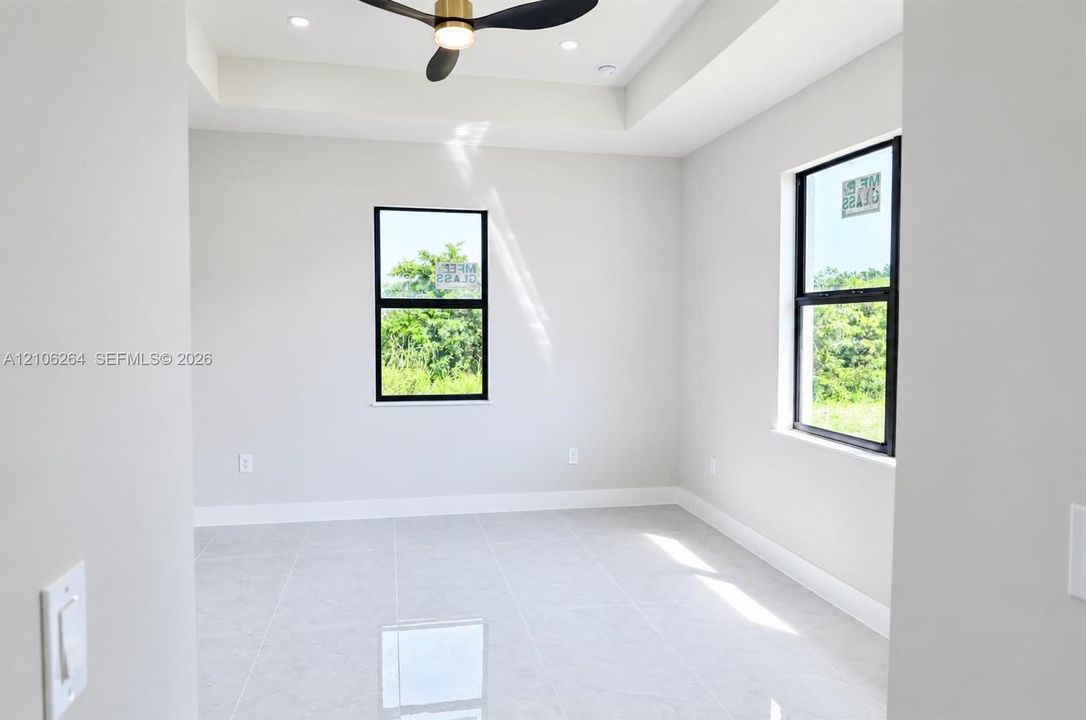 Room featuring neutral tile flooring, a tray ceiling, recessed lighting, a modern ceiling fan, and black-framed windows