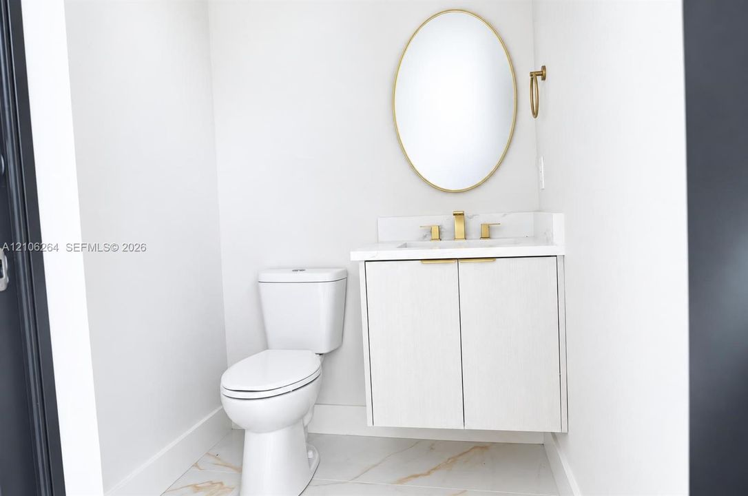 Floating vanity with integrated countertop and backsplash, brass-toned hardware, oval-framed mirror, and large-format tile flooring