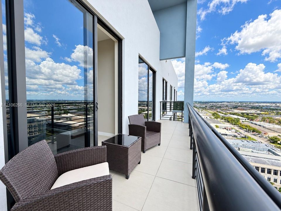 Covered balcony featuring large-format porcelain tile flooring, black metal railing, and expansive floor-to-ceiling glass sliding doors