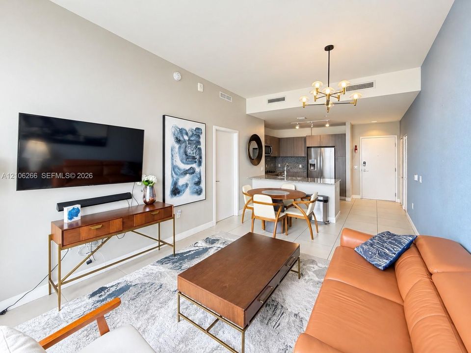 Open-concept interior featuring light-toned tile flooring, modern multi-arm chandelier lighting, stone-top breakfast bar, and flat-panel cabinetry