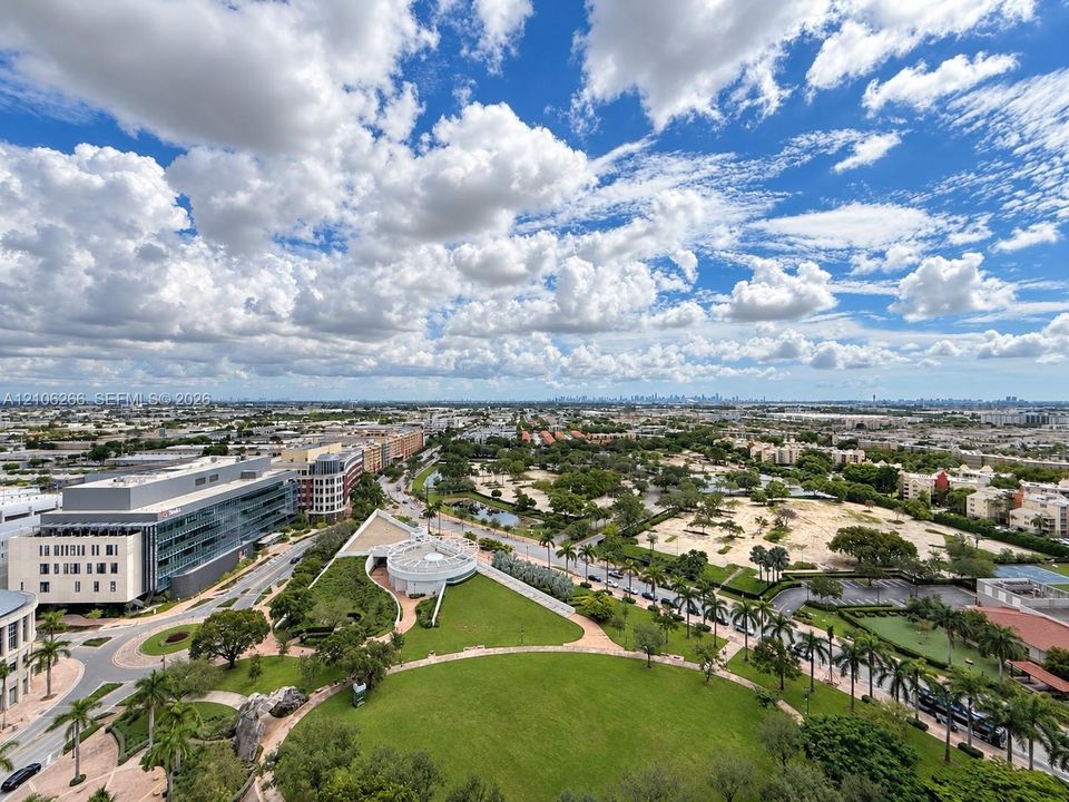 Elevated cityscape perspective featuring expansive green spaces, paved pedestrian walkways, mature palm trees, and professional office architecture