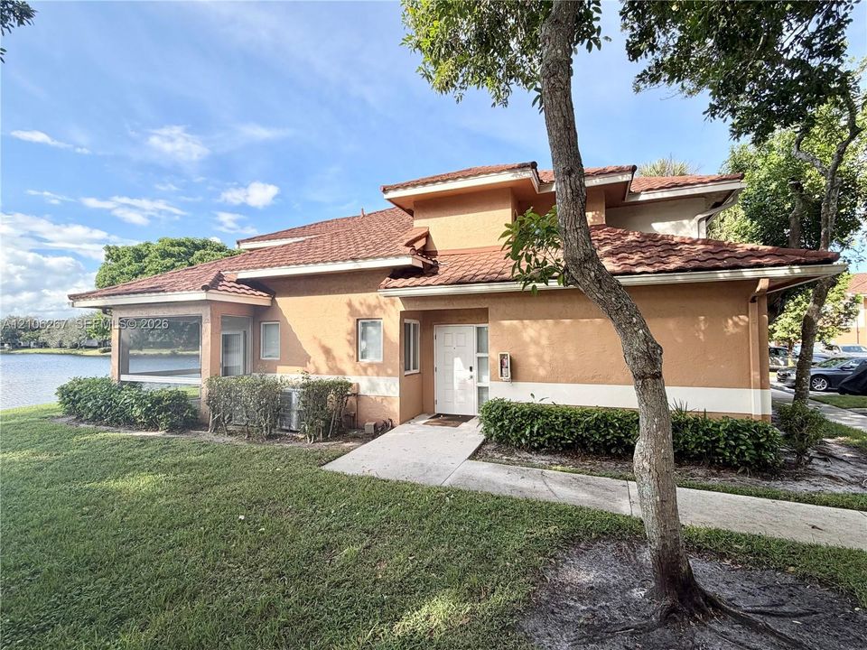 Two-story stucco exterior featuring a tiered tile roof, screened-in enclosure, and waterfront positioning