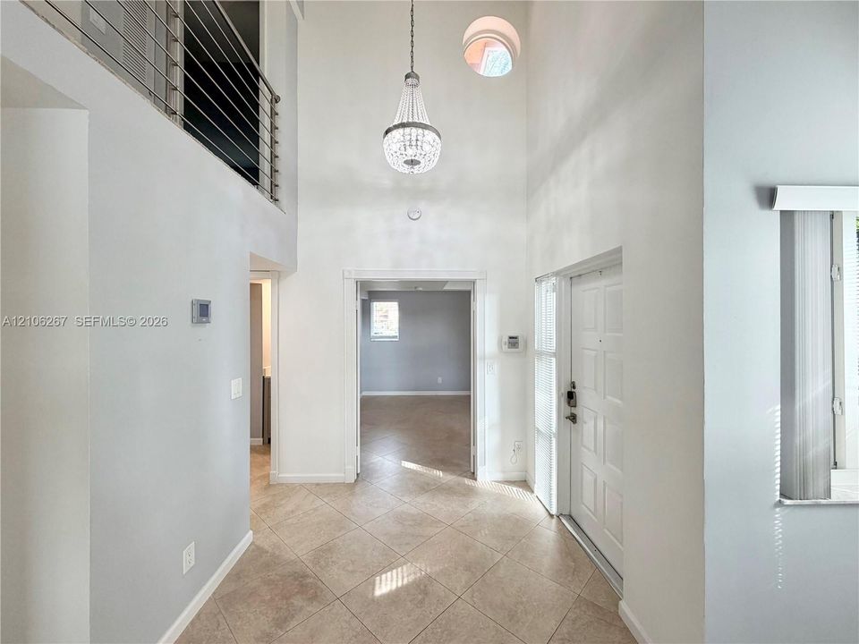 Double-height ceiling entryway featuring tiled flooring, a decorative chandelier, an architectural circular window, and a metal horizontal-bar railing