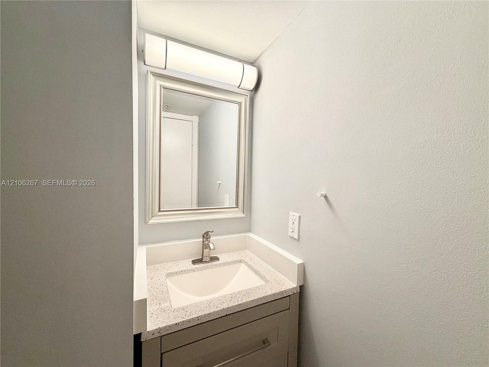 Single-sink vanity with speckled stone-finish countertop, undermount basin, brushed metal faucet, framed mirror, and horizontal wall-mounted light fixture