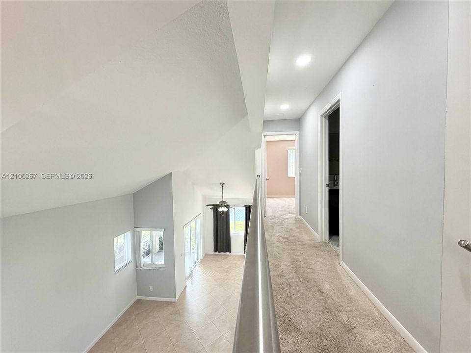 Open mezzanine featuring a metal railing, neutral carpeting, recessed ceiling lighting, and vaulted ceilings