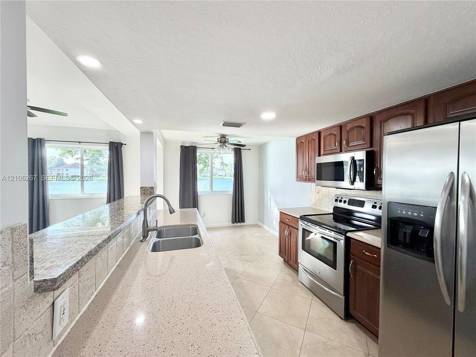 Kitchen featuring a stone-composite breakfast bar with an undermount dual-basin sink, wood-finish cabinetry, stainless steel appliances, and tile flooring
