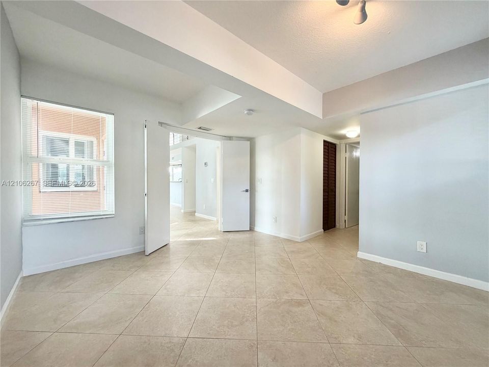 Interior space featuring large-format ceramic tile flooring, neutral wall tones, multi-pane window with interior blinds, and ceiling-mounted lighting fixtures
