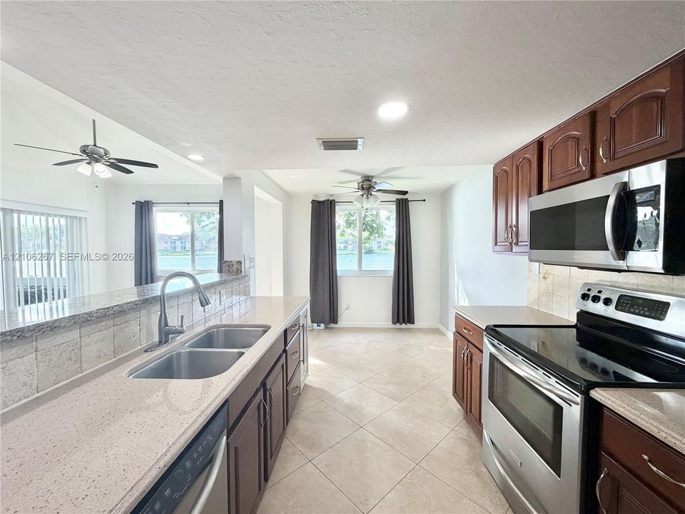 Kitchen featuring raised-panel wood cabinetry, stone countertops, stainless steel appliances, double-basin sink with arched faucet, and tile flooring