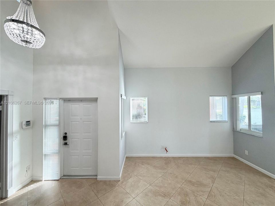Entryway featuring high vaulted ceilings, oversized tile flooring, a crystal chandelier, neutral wall tones, and windows with horizontal blinds