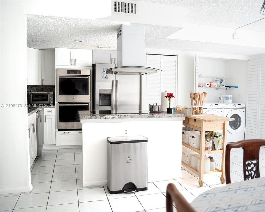 Kitchen featuring white cabinetry, stone-finish countertops, stainless steel wall-mounted double oven, overhead exhaust hood, and white tile flooring