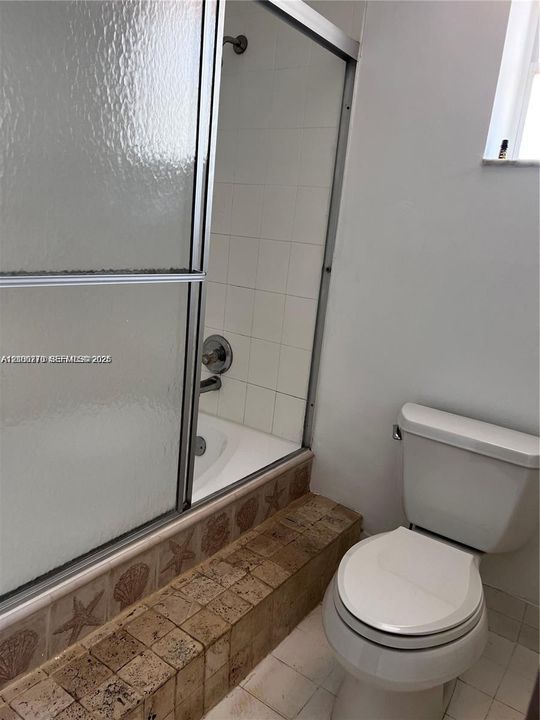 Bathtub and shower combination featuring a metal-framed glass enclosure, white wall tiling, and a decorative tile surround with a coastal motif