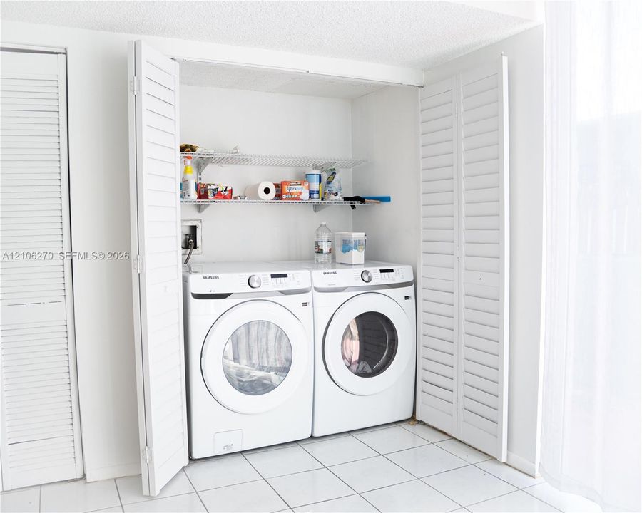 Laundry alcove featuring white louvered bifold doors, tile flooring, and integrated metal wire shelving