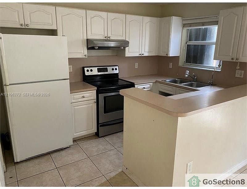 Kitchen featuring white shaker-style cabinetry, stainless steel range with overhead hood, dual-basin sink, laminate countertops, and ceramic tile flooring
