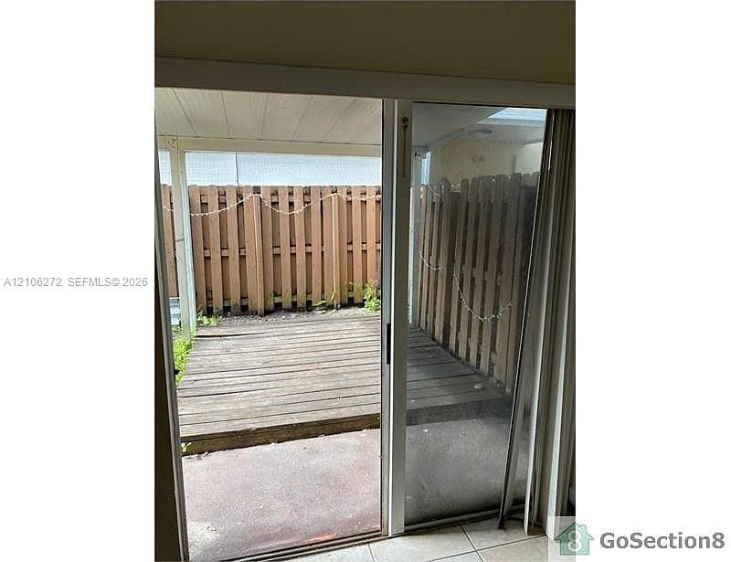 Sliding glass door opening to a private outdoor space featuring a wood-plank deck, covered patio area, and wood privacy fencing