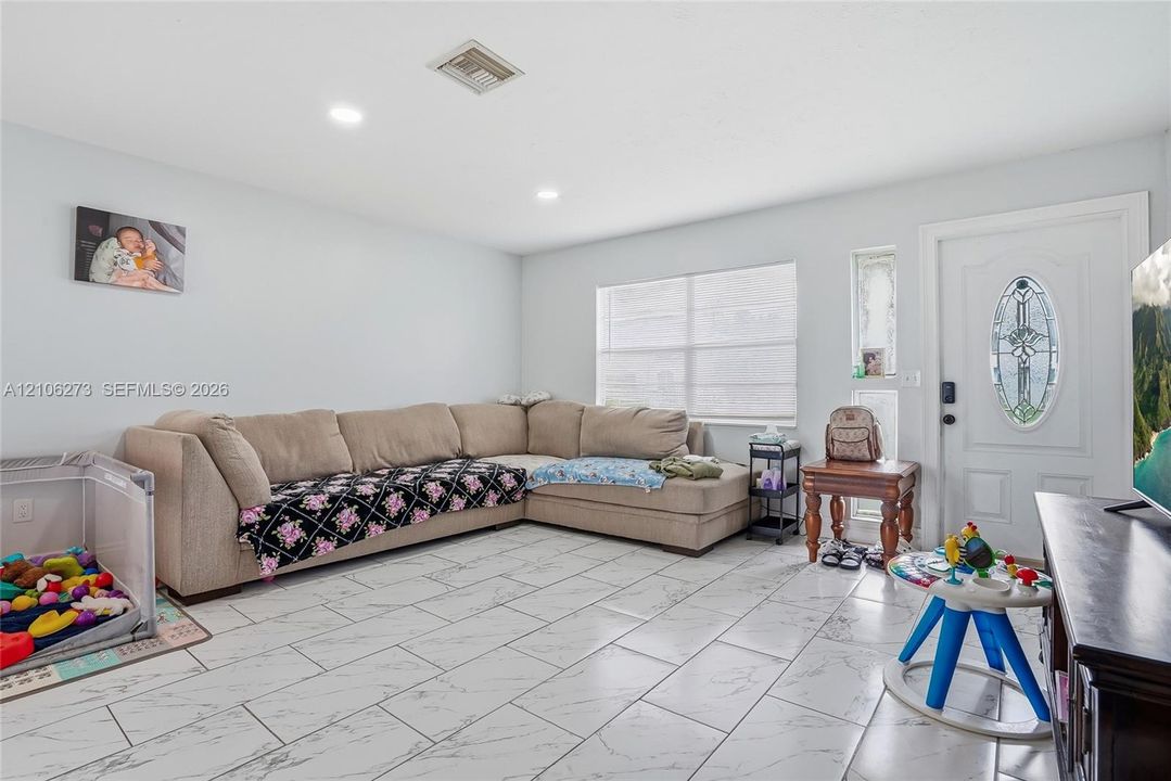 Living area featuring large-format tile flooring with marble-style veining, recessed lighting, and a front entry door with a decorative oval glass insert