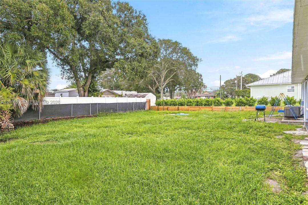 Expansive backyard featuring a sprawling lawn, white vinyl perimeter fencing, and mature trees