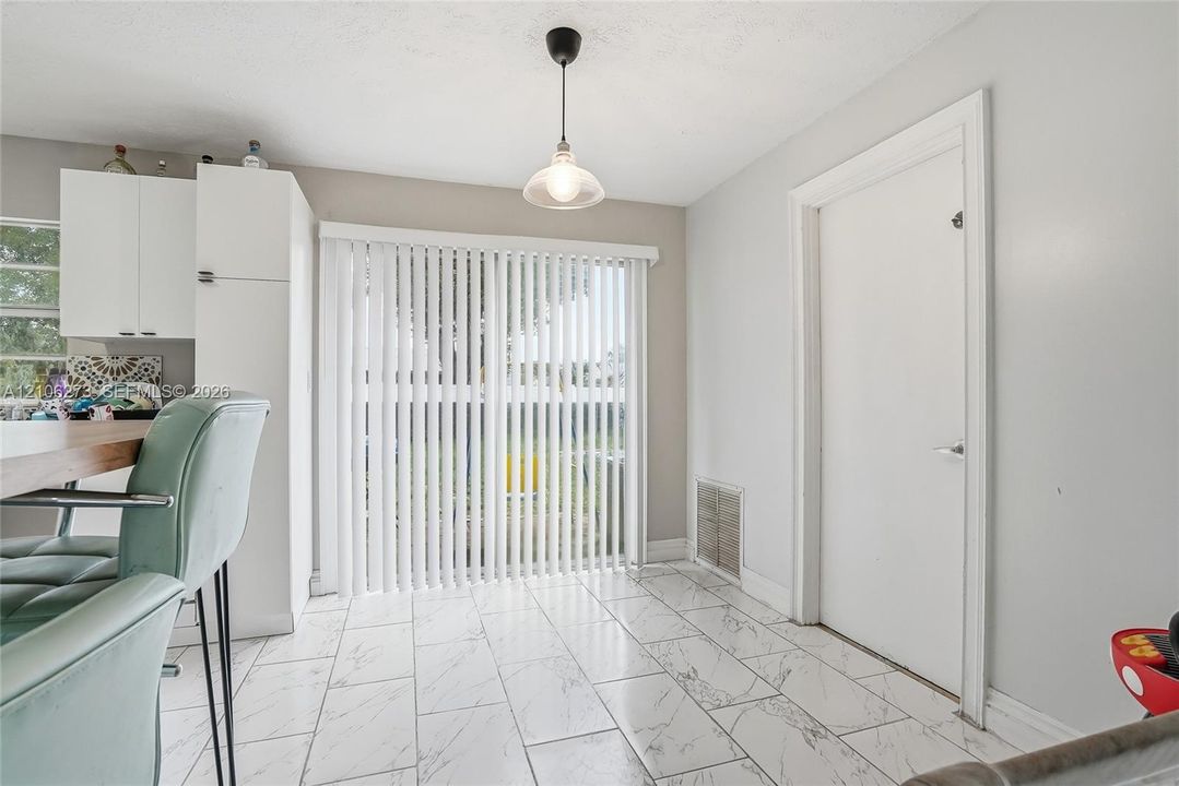 Interior space featuring large-format tile flooring with a neutral veined pattern, floor-to-ceiling sliding glass doors, white cabinetry, and a single pendant light fixture