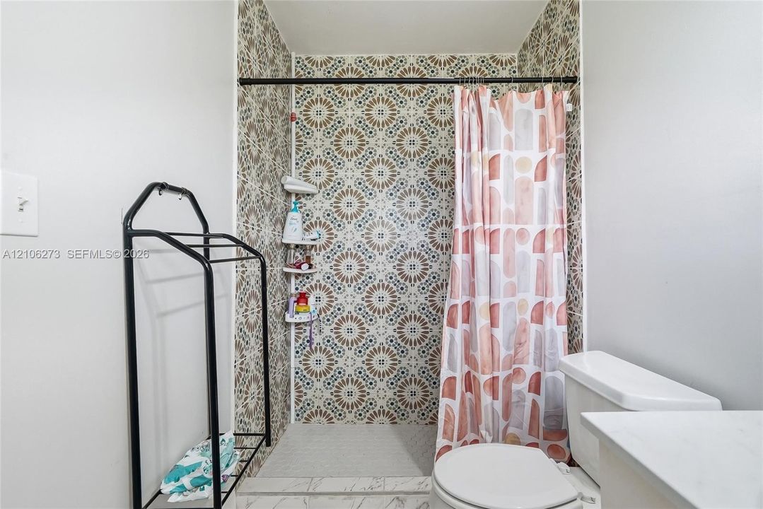 Walk-in shower featuring patterned tile walls, built-in shelving, and a matte black shower curtain rod