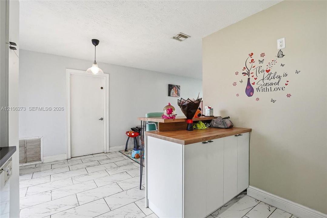 White cabinetry with wood-finish countertop, white tile flooring, and pendant lighting